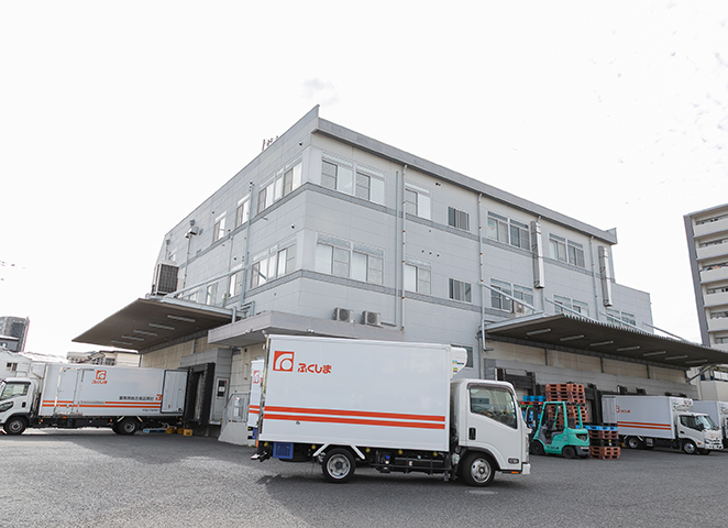 数台のトラックが停まっている大きな白い建物の外観。