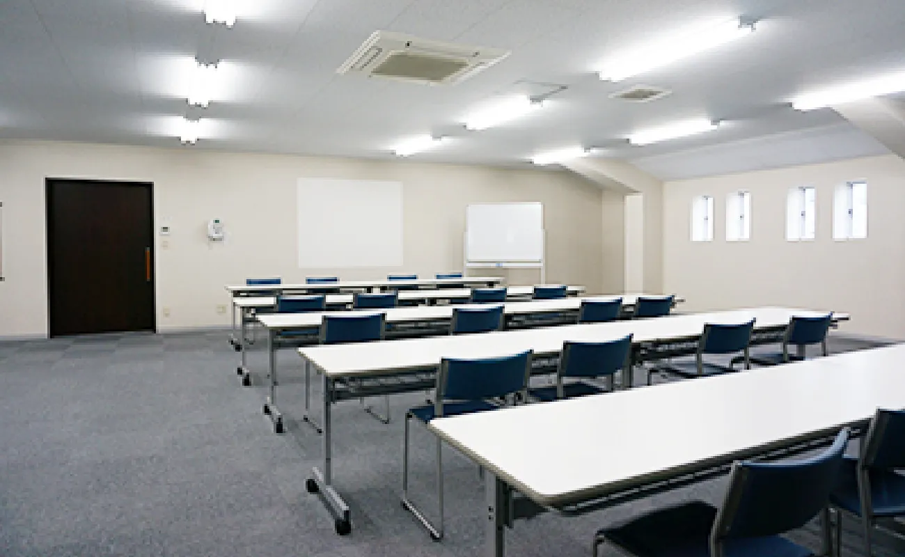 テーブルと椅子が並ぶ広い空の部屋の様子。