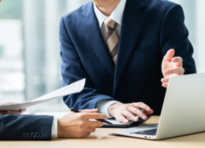 二人のビジネスパーソンがテーブルに座り、ノートパソコンを使っている様子。