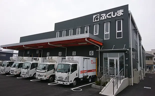 大きな倉庫の前に数台のトラックが駐車されている様子を示す画像